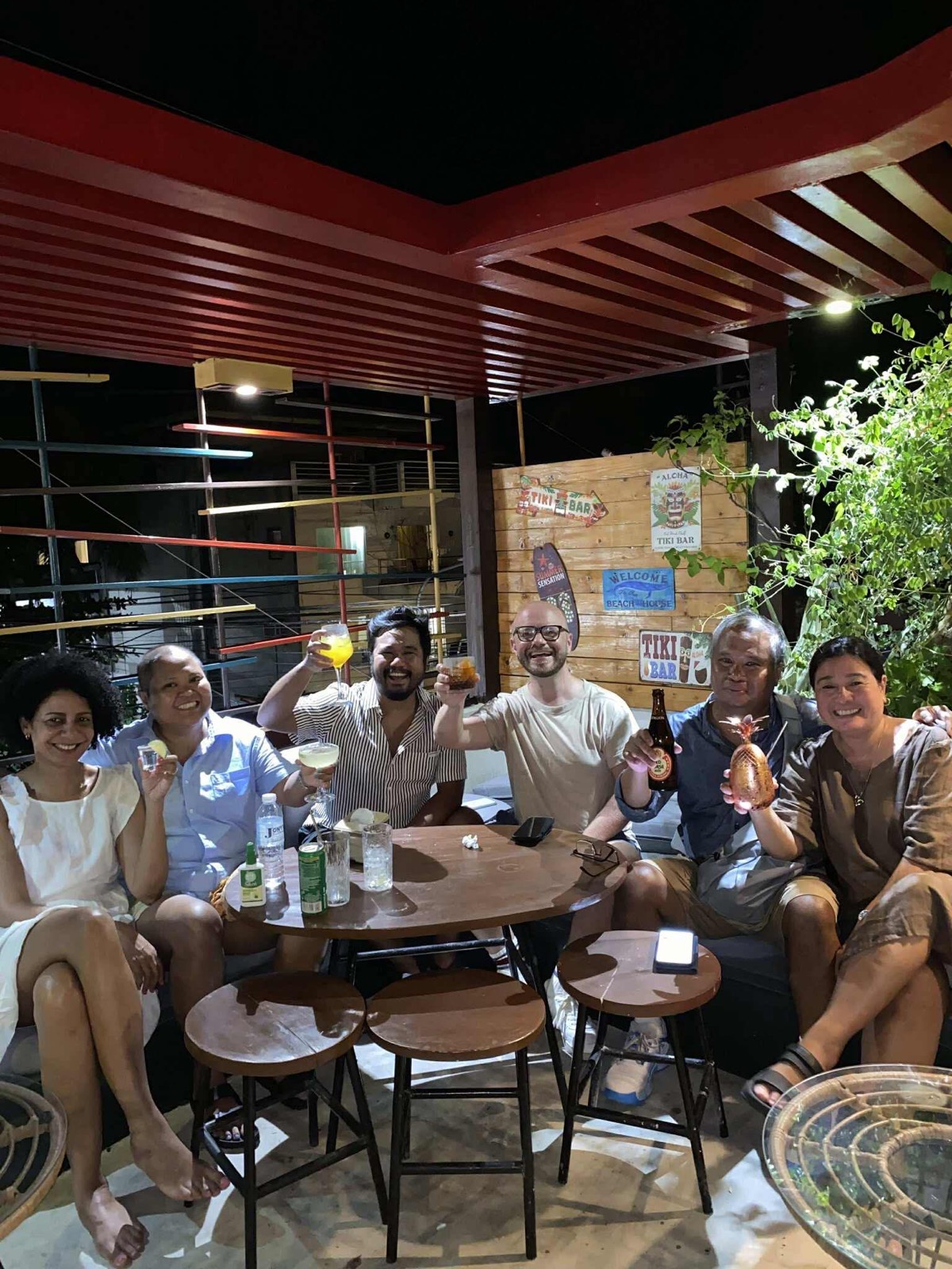 A mixed group of guests raising their drinks together on Mai Tai's rooftop bar at night