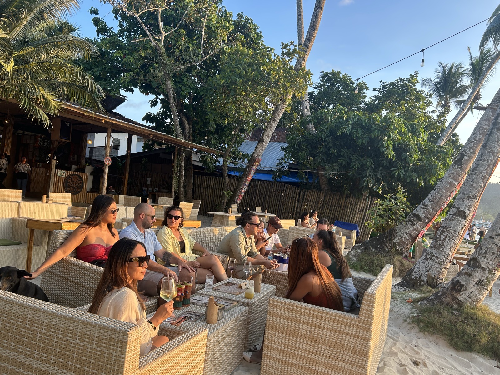 Golden-hour crowd lounging in rattan sofas under the palms at Mai Tai Port Barton